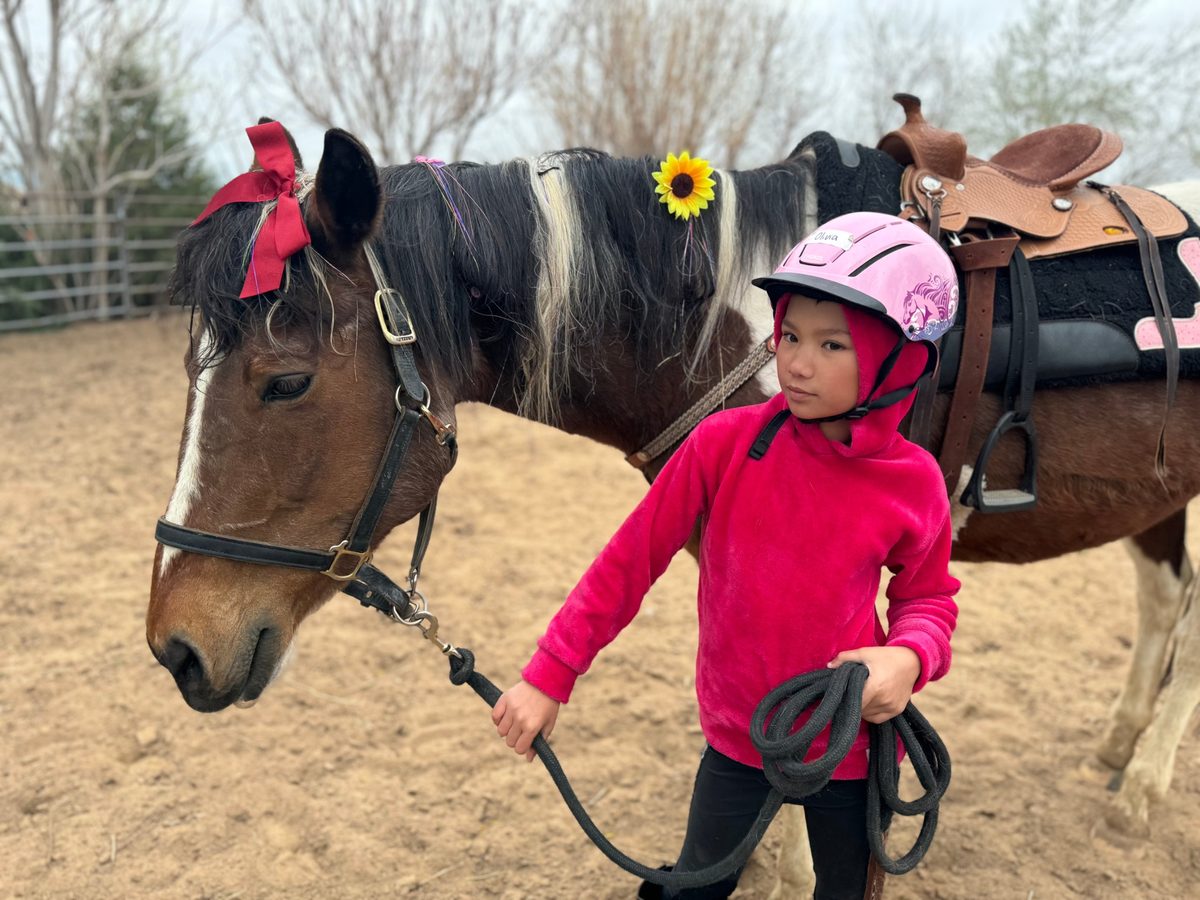 Young rider Olivia in a pink helmet leading Bourbon, dressed up with a red bow and a sunflower
