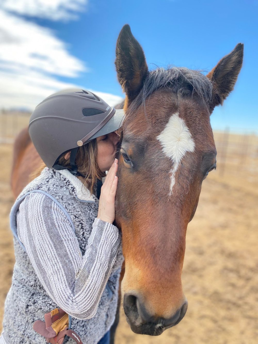 A rider in a helmet giving Champion, a bay horse with a white star, a gentle kiss